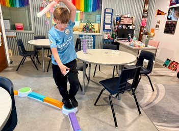 A student walks along a curved balance path laid out across the classroom floor.