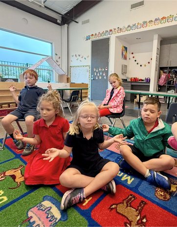 Students sitting cross-legged in a circle on the classroom floor during a lesson.
